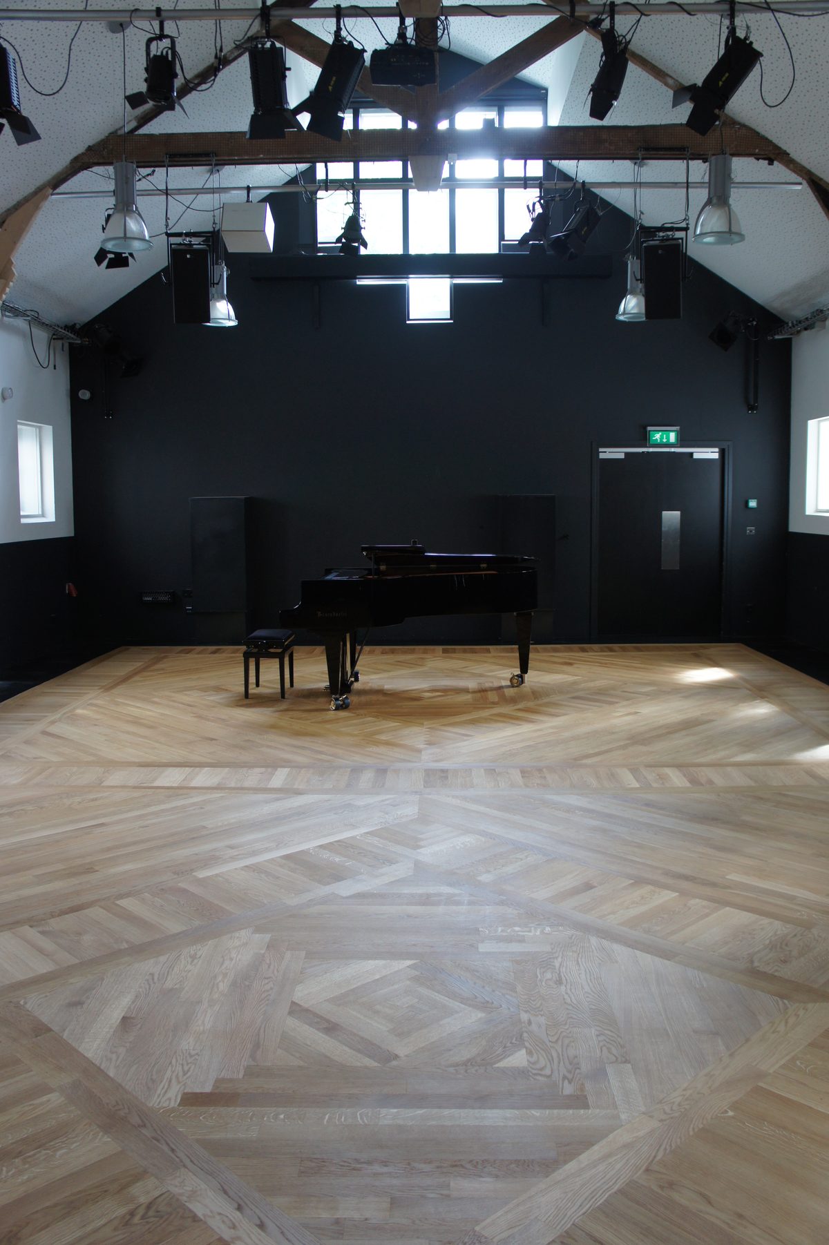 Maatwerk parketvloer met geometrisch patroon in een zaal met vleugel